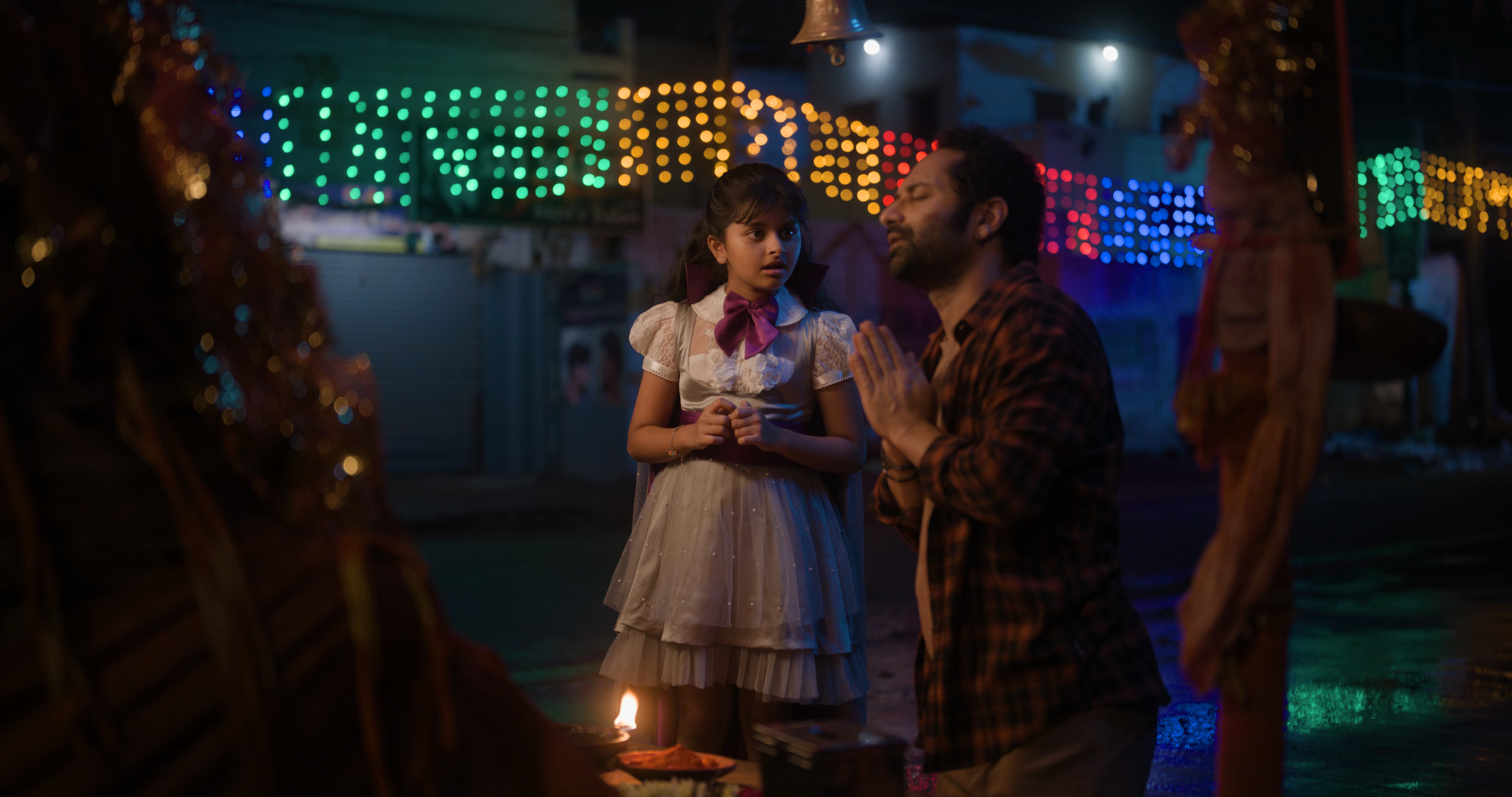 Fahadh Faasil and Ssara Palekar in a low-light night scene from Don’t Trouble the Trouble, surrounded by colorful lights, with a small flame in the foreground. Still from the final Malayalam version.